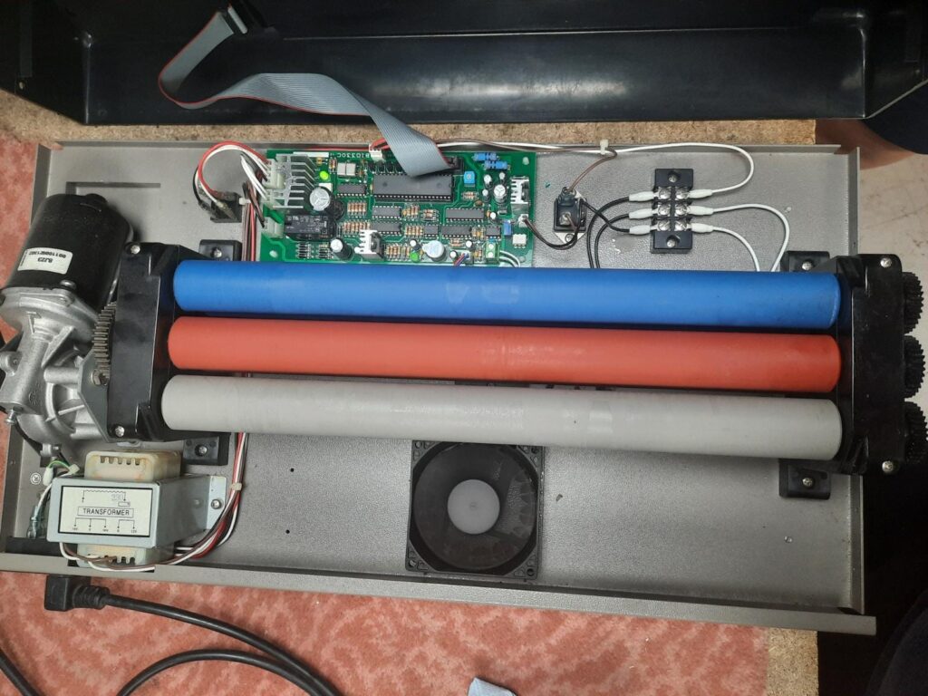 The inside of pouch laminator, you can see the electrics, fan, gears and three heated rollers.