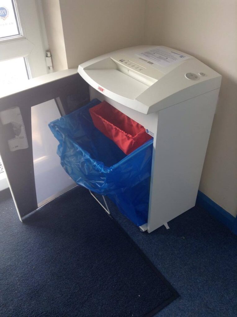 Image of a HSM shredder in a office with the door open so you can see the blue shredding bag underneath.